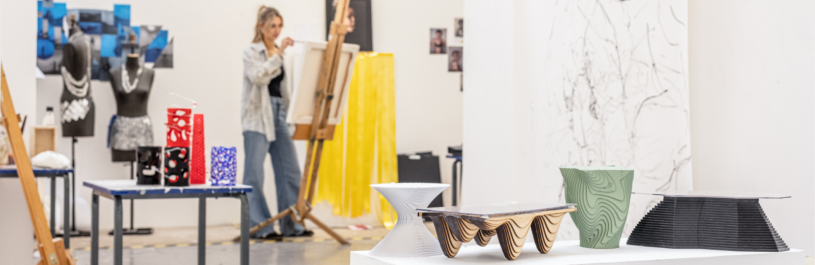 3D models in the foreground with a female student painting on an easel in the background