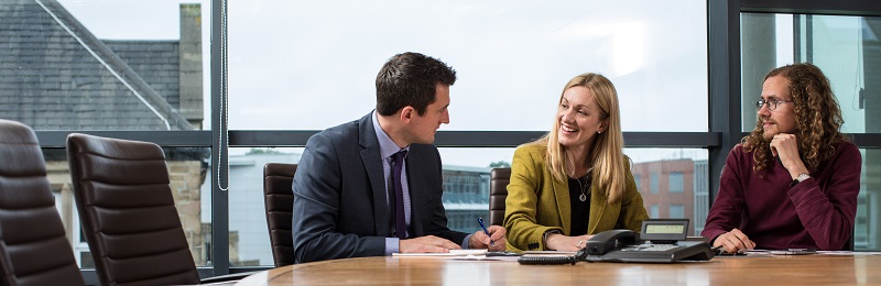 Three people in discussion around boardroom table