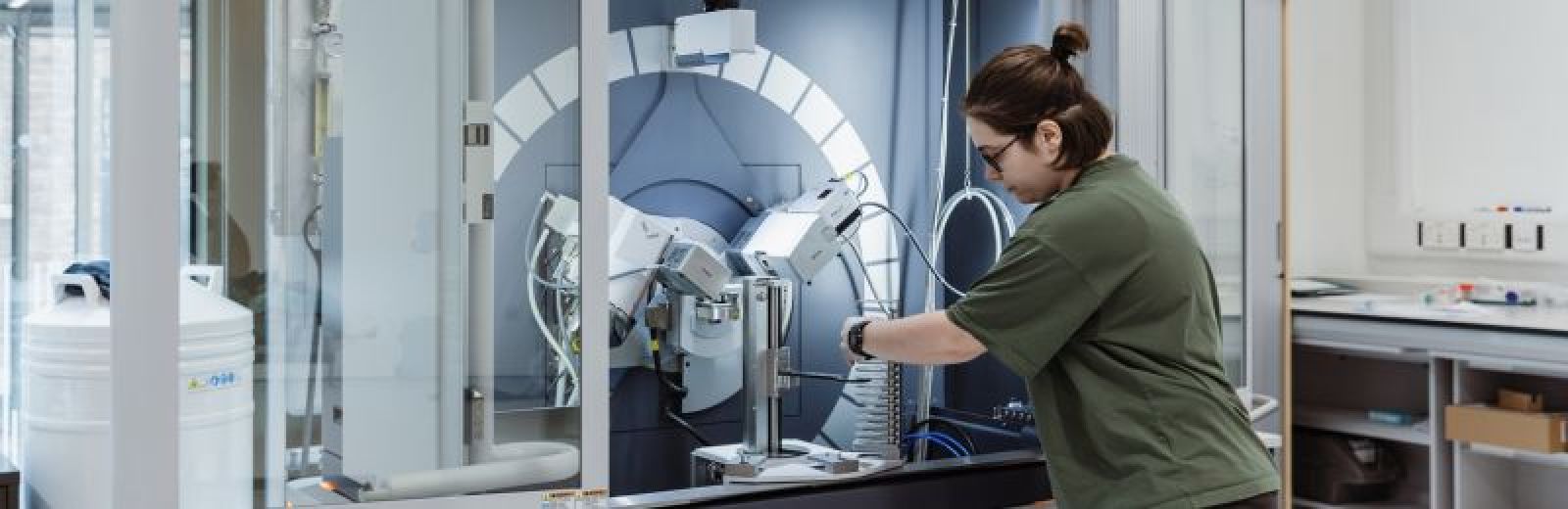 A student, wearing a green t shirt, is loading a sample in to a x-ray diffractometer.