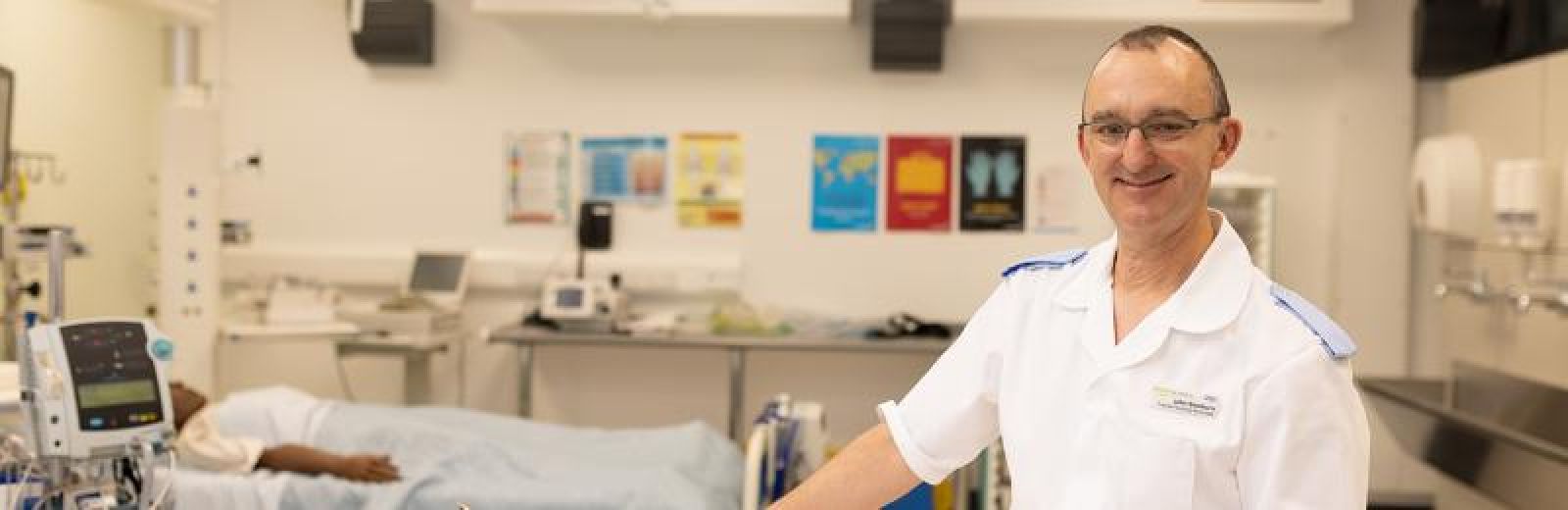 A student in a nursing uniform with a mannequin doll in a patient's bed behind them.