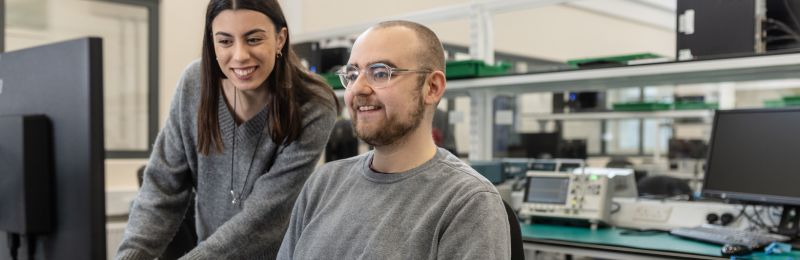 A cropped image of two students sat at a work bench looking at a screen in an electrical engineering lab at the University of Leeds.