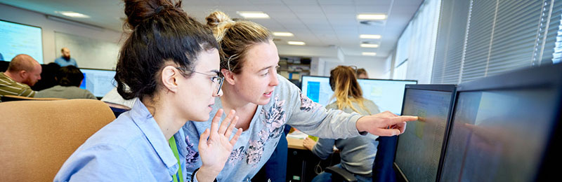 Two female students looking and a computer screen, one is pointing