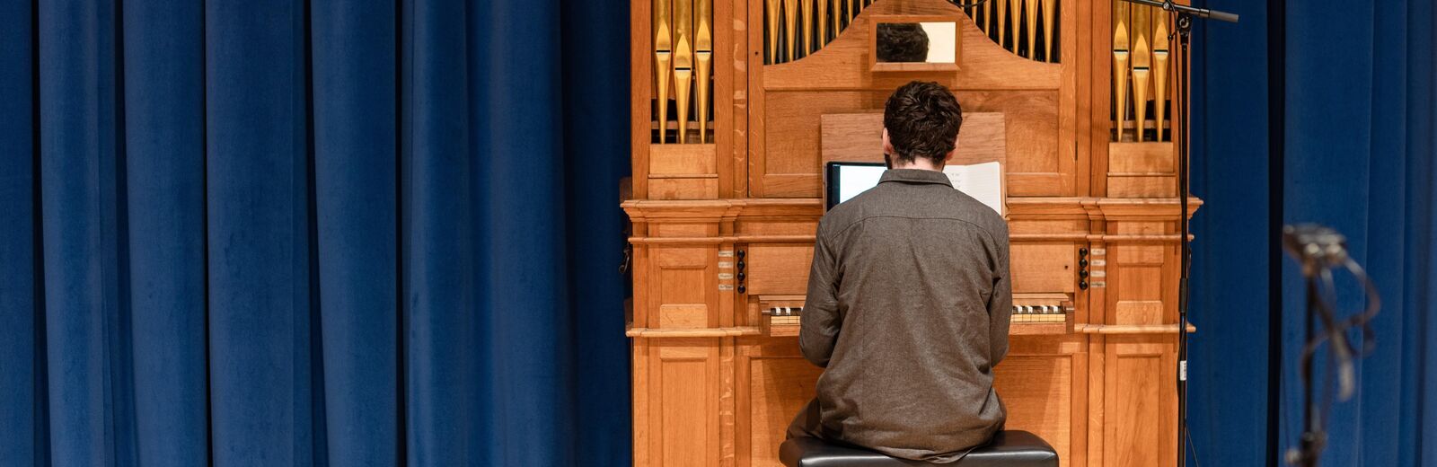 Postgraduate student in the School of Music. They are performing on the organ in the Concert Hall, their back is to the camera. Behind the organ is a royal blue velvet curtain.