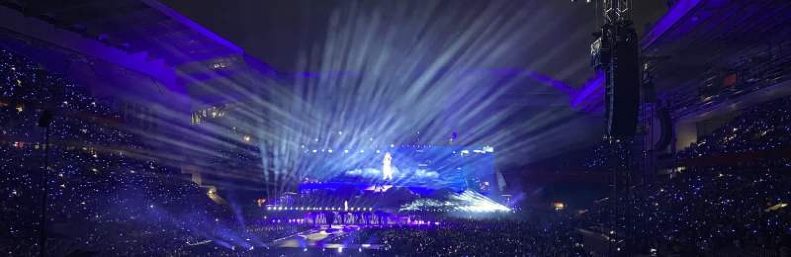 Live music performance in large venue with audience, laser lights and performer on stage
