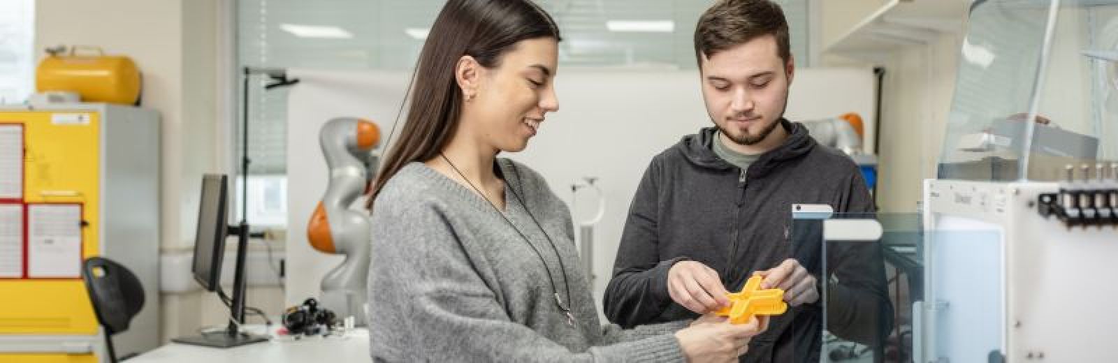 Two students retrieving a yellow 3d printed part for an electronics project.