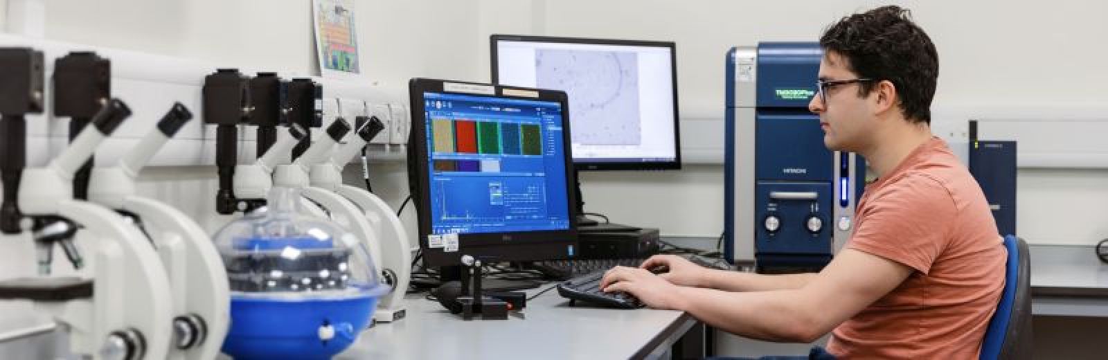 A materials science student sat at a desktop computer with the results of an experiment on the screen displaying different colour materials.