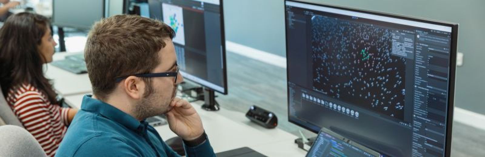 Two computer science students sat working at desktop computers. Their screens show different cloud computing models in action.