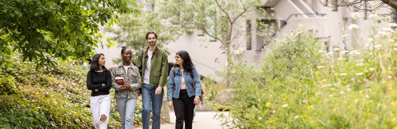 Four students walk through campus together, the Roger Stevens building in the background.