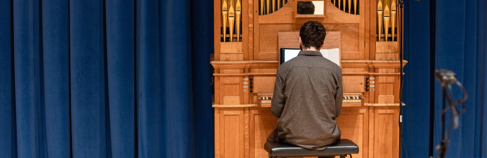 Postgraduate student in the School of Music. They are performing on the organ in the Concert Hall, their back is to the camera. Behind the organ is a royal blue velvet curtain.